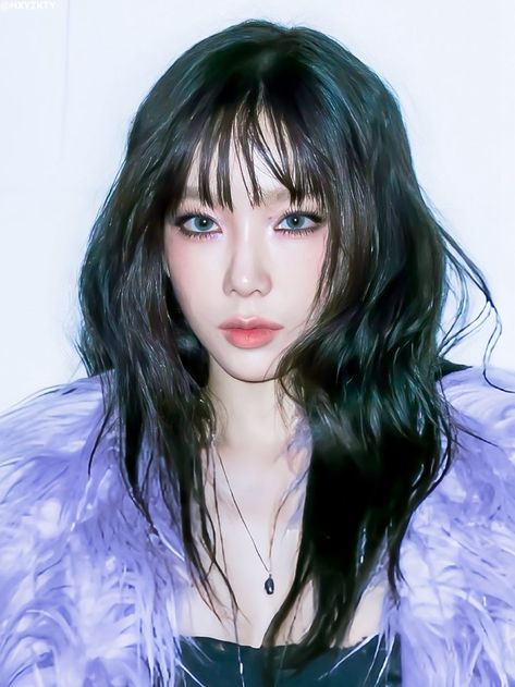 This  contain an image of Taeyeon with long black hair and blue eyes wearing a purple fur coat, posing for the camera