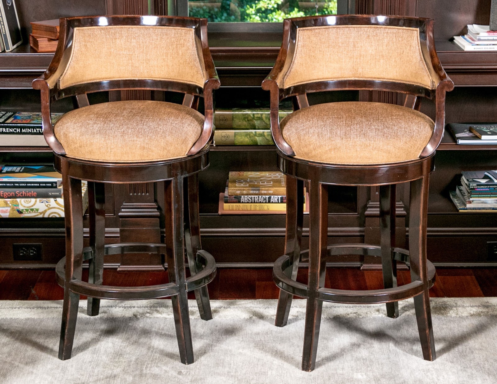 A pair of bar stools with silk chenille upholstery in front of built-in library shelves