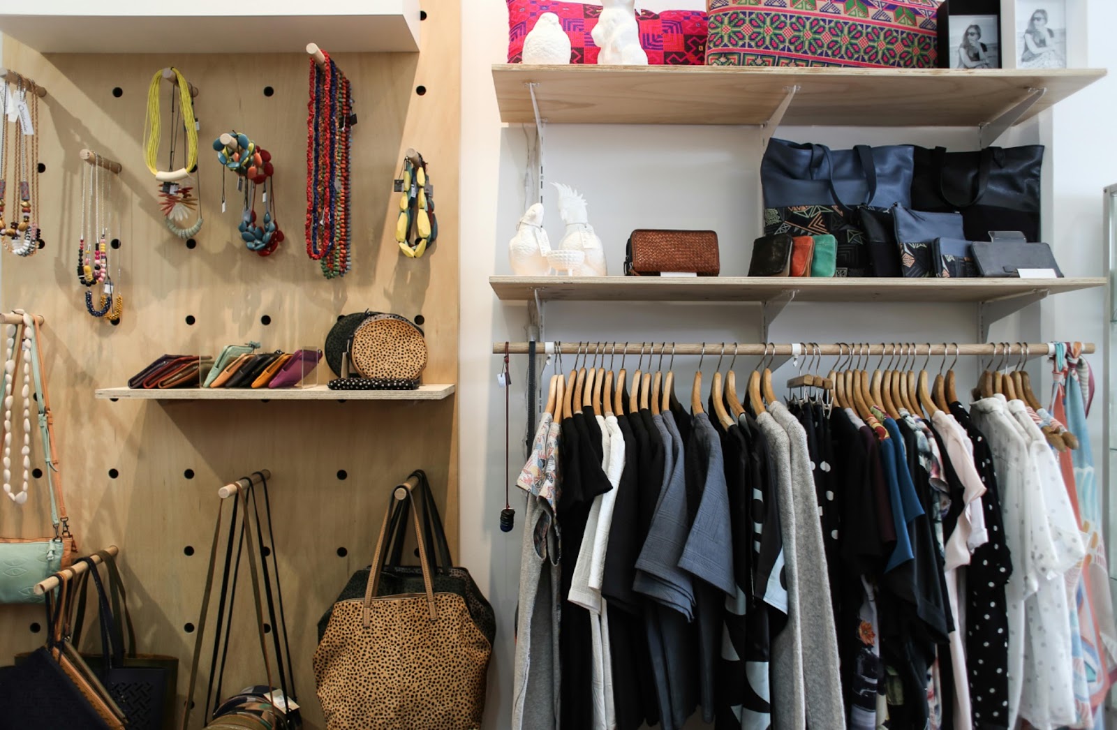 An organized closet with pegboard for accessories, shelves for bags and wallets, and clothes hanging on wooden hangers.