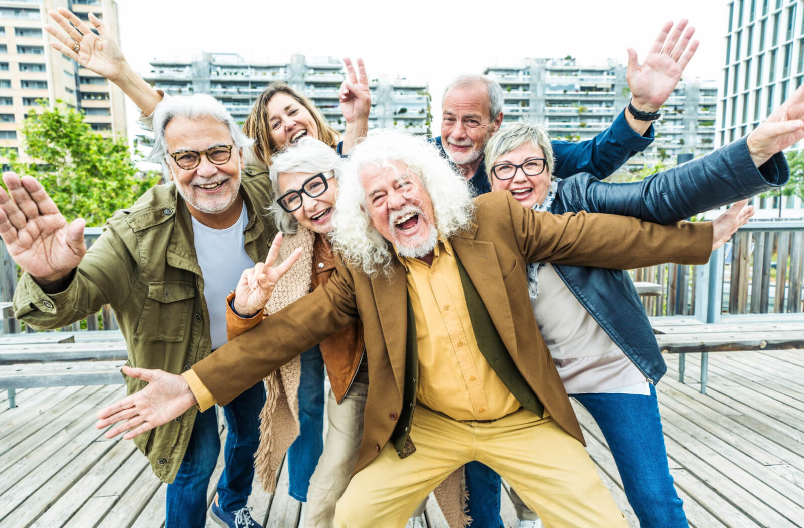 A group of 6 older adults posing on a bridge for a photo, arms outstretched and laughing together in Birmingham.