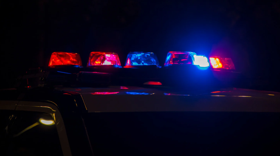 (Police car with flashing red and blue lights at night, symbolizing law enforcement presence and potential civil rights concerns during police interactions.)