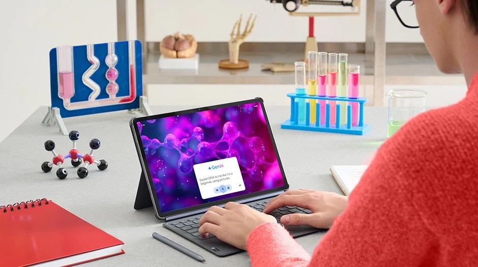 A person sits at a desk covered with science supplies, using a Lenovo Idea Tab Pro tablet in Luna Grey with a Folio Case, 2-in-1 Keyboard Pack, and Lenovo Tab Pen Plus to engage with Google Gemini