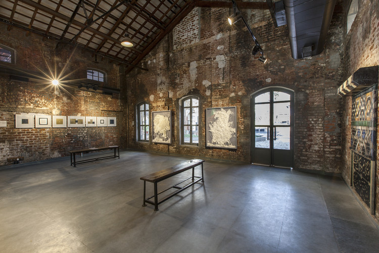 A rustic art gallery room with exposed brick walls and high ceilings showcases framed artwork is a part of an industrial adaptive reuse.