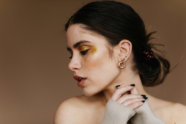 Fascinating woman with party makeup posing . Indoor close-up photo of relaxed brunette girl wears earrings.