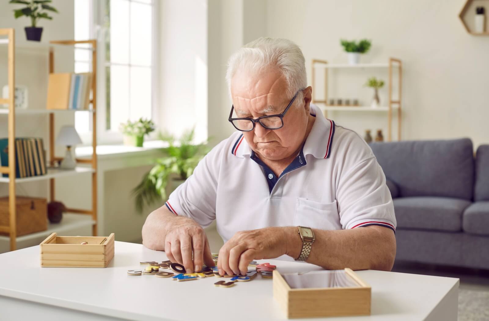 A senior seated at a table frowns as they sort alphabet pieces of a puzzle