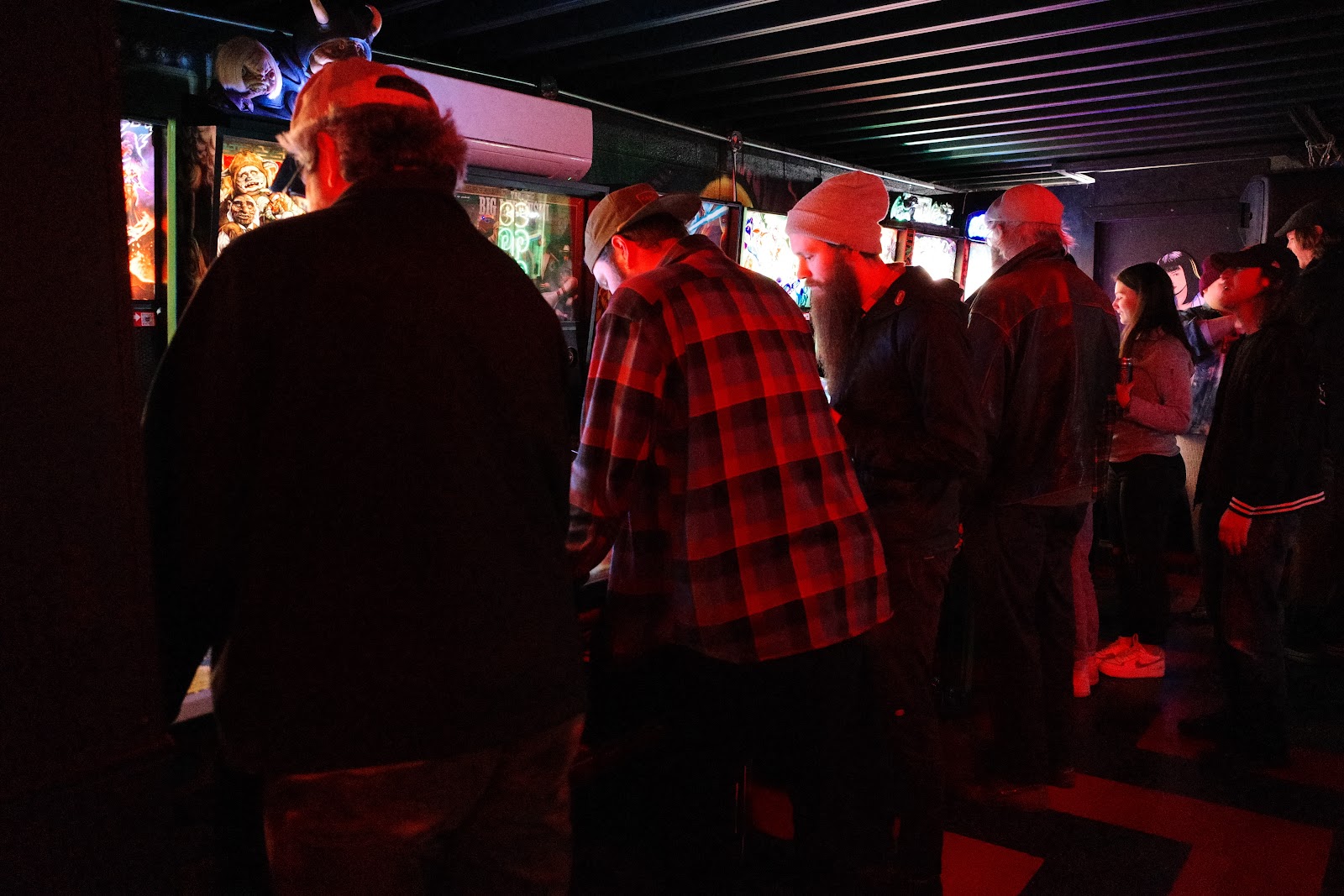 People playing pinball in a dimly lit bar.