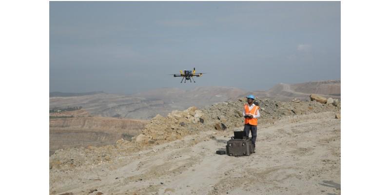 A person in a helmet and orange vest with a drone flying over a desert

Description automatically generated