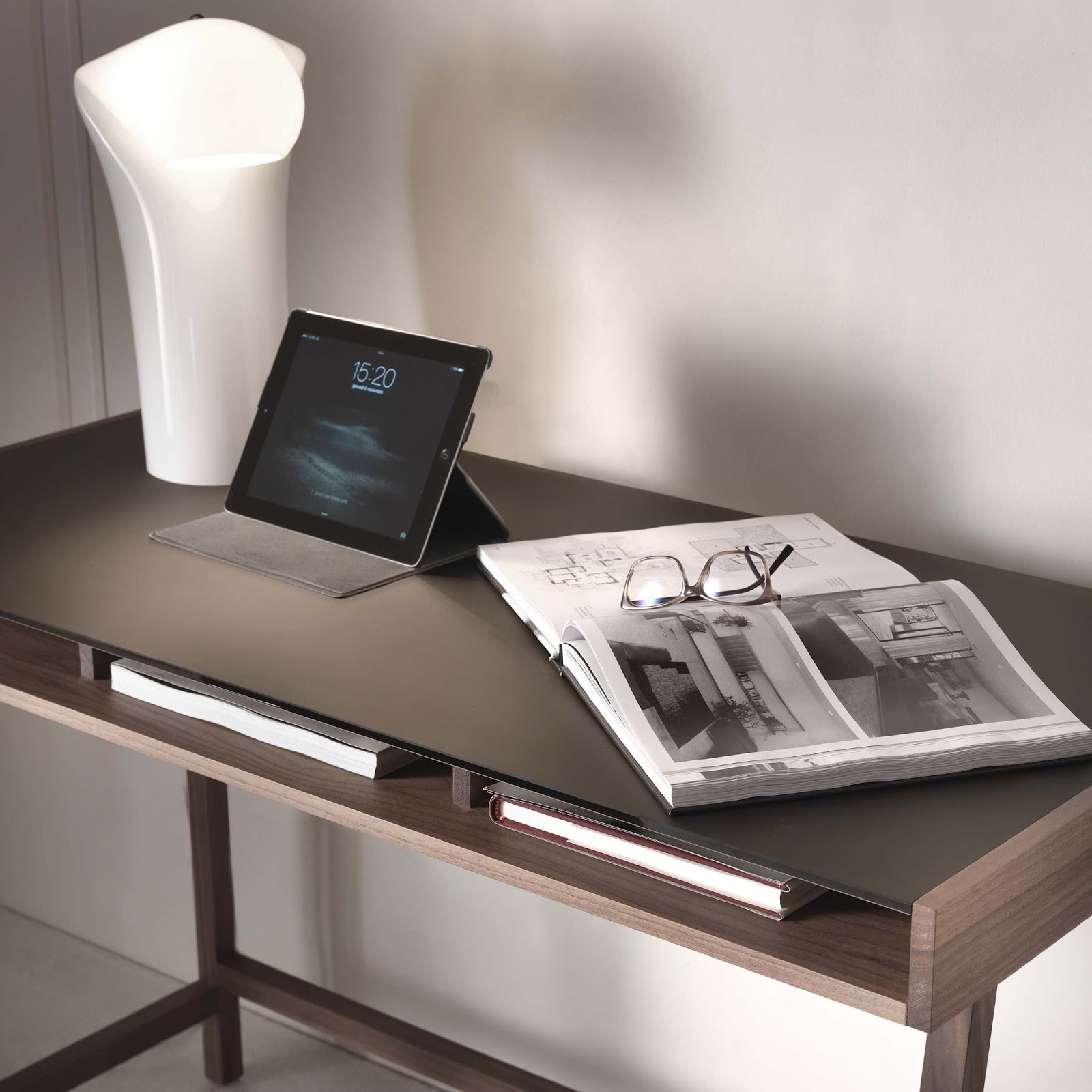 Minimalist walnut home office desk with integrated storage, styled with a sculptural white lamp, tablet, and design magazines.