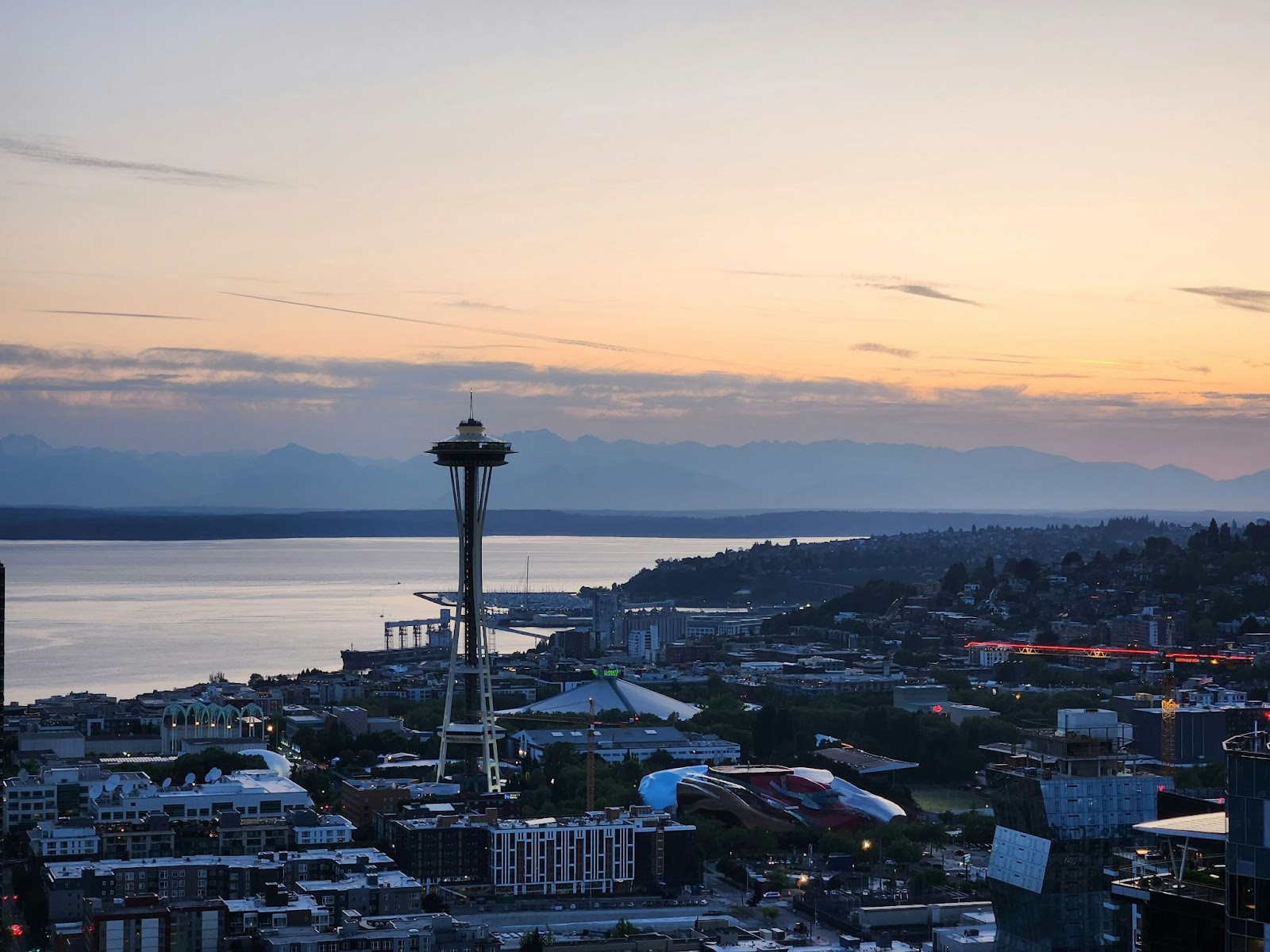 Photo of space needle at twilight, the city below with a mountain range and clouds behind