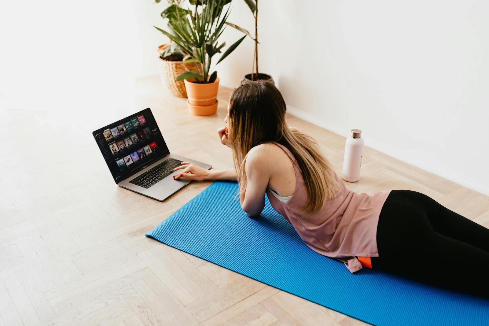 Adaptación a las nuevas tendencias del sector: foto mujer joven tumbada en el suelo sobre una esterilla azul mientras usa el notebook portátil en casa