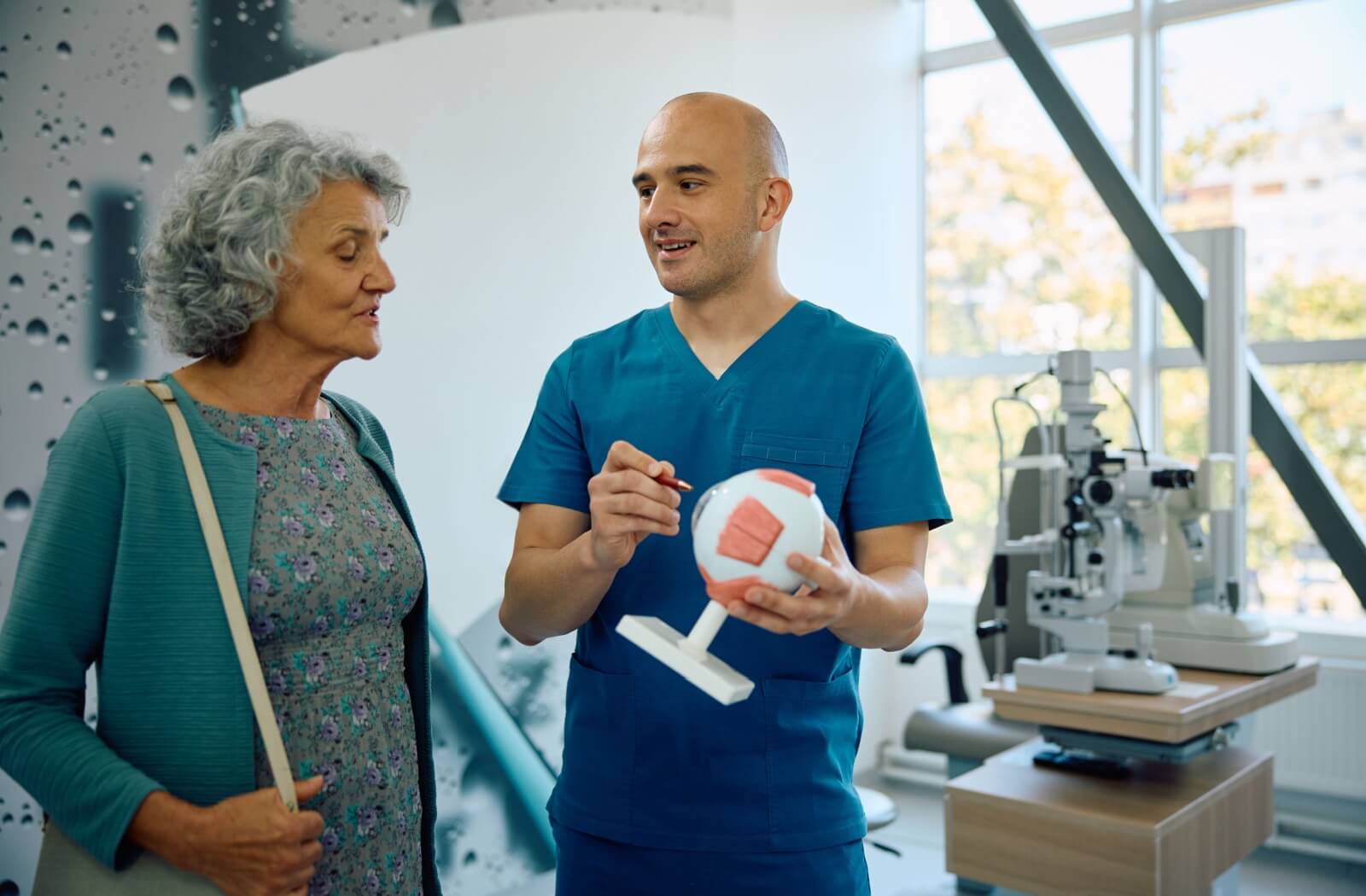 A person listening to an eye doctor as they explain something and point to a large model eye