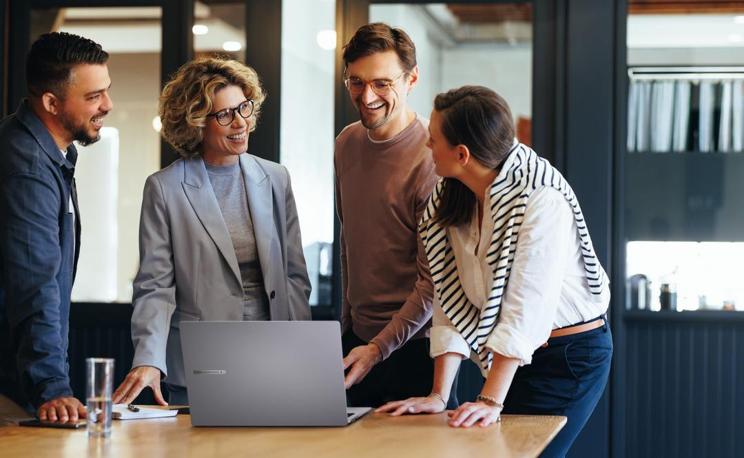 Quatro pessoas no escritório conversam ao redor de um notebook corporativo em ambiente moderno.