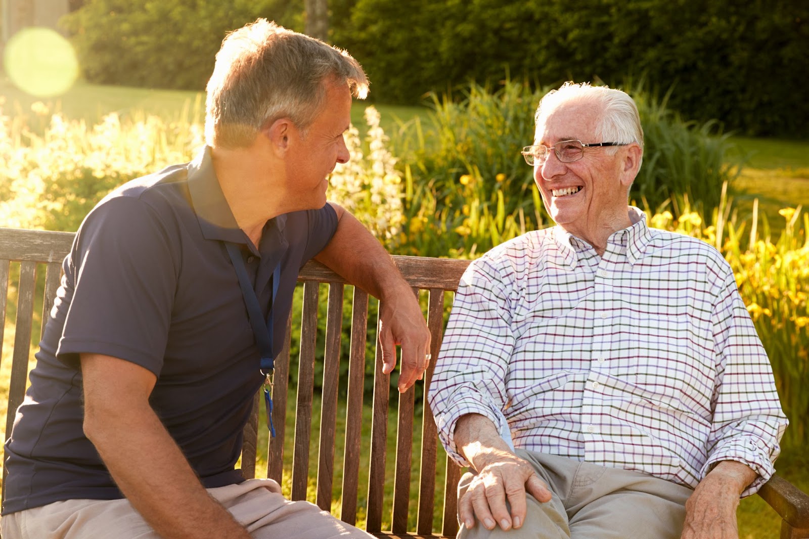 A senior and his adult son spending an afternoon visiting outside in the sun.