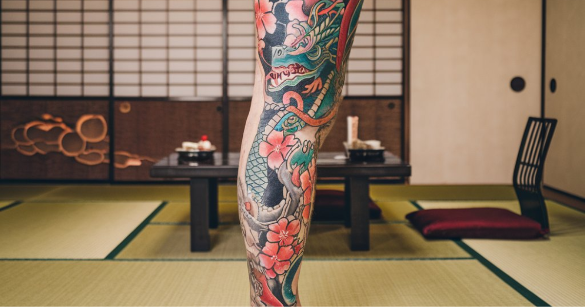 A person showcasing a Japanese leg sleeve tattoo in a traditional Japanese-style room, highlighting intricate designs.