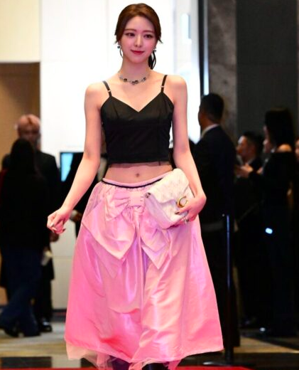 This contains an image of ITZY Yuna on a  black cropped tank top and a pink skirt looking beautiful