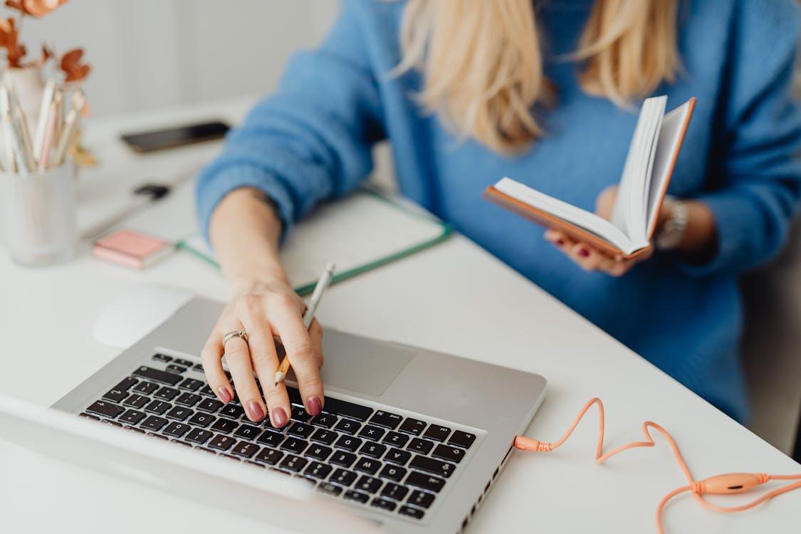 Free Person Holding a Notebook While Using a Laptop Stock Photo