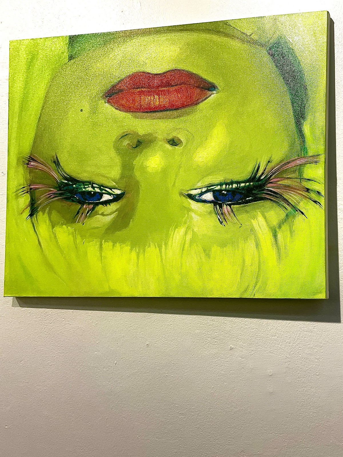 Green painting of a facial outline with emphasized blue eyes and red lips.
