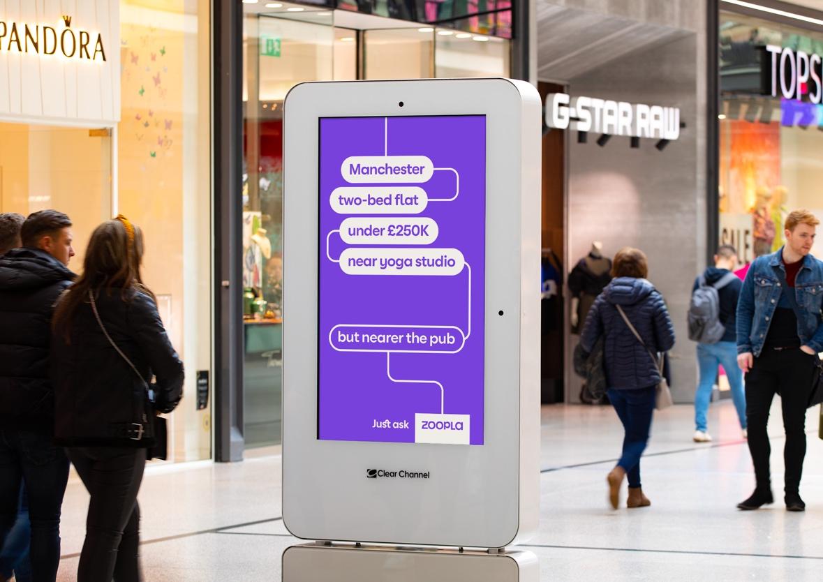 A person standing in a mall with a digital screen Description automatically generated