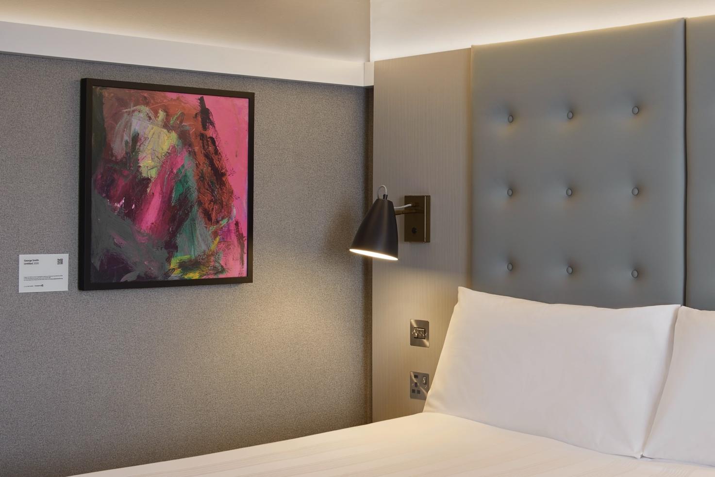 A bed with a lamp and a painting on the wall Description automatically generated