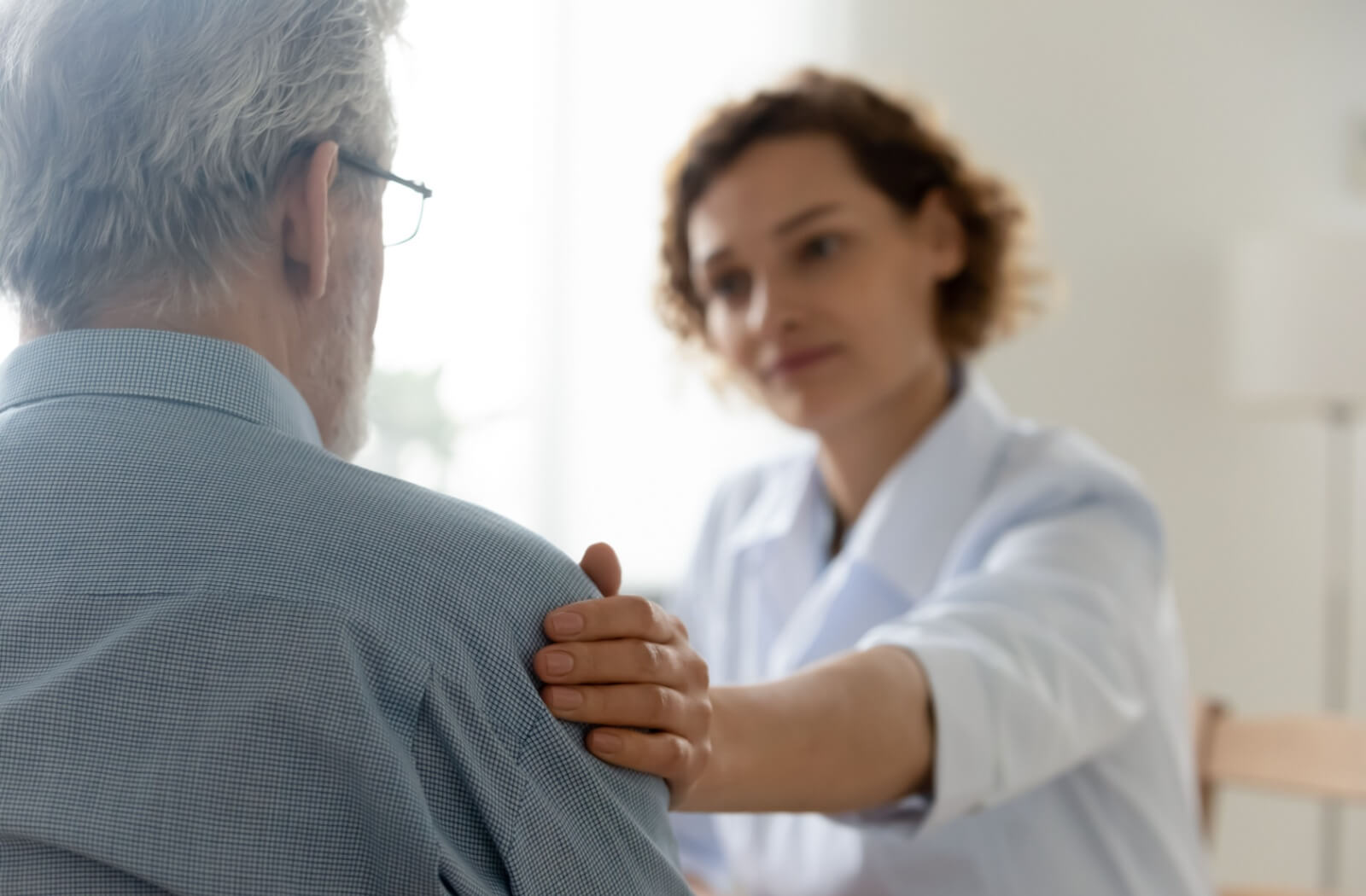 An adult child rests their hand on their parent's shoulder to reassure them of their presence.