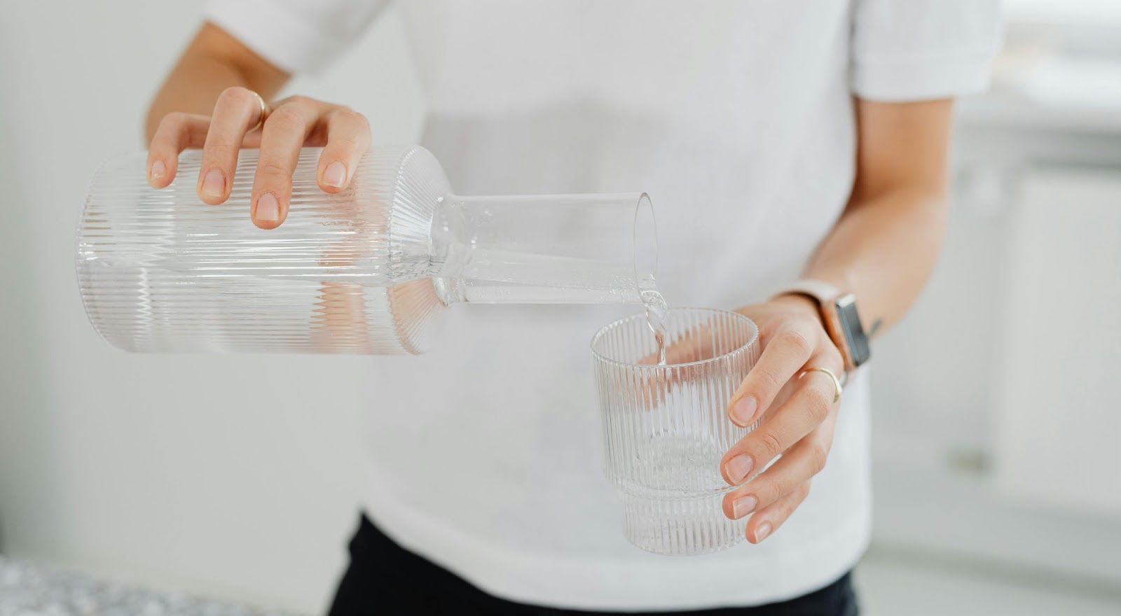 Adult person pours water from a pitcher into a glass to drink