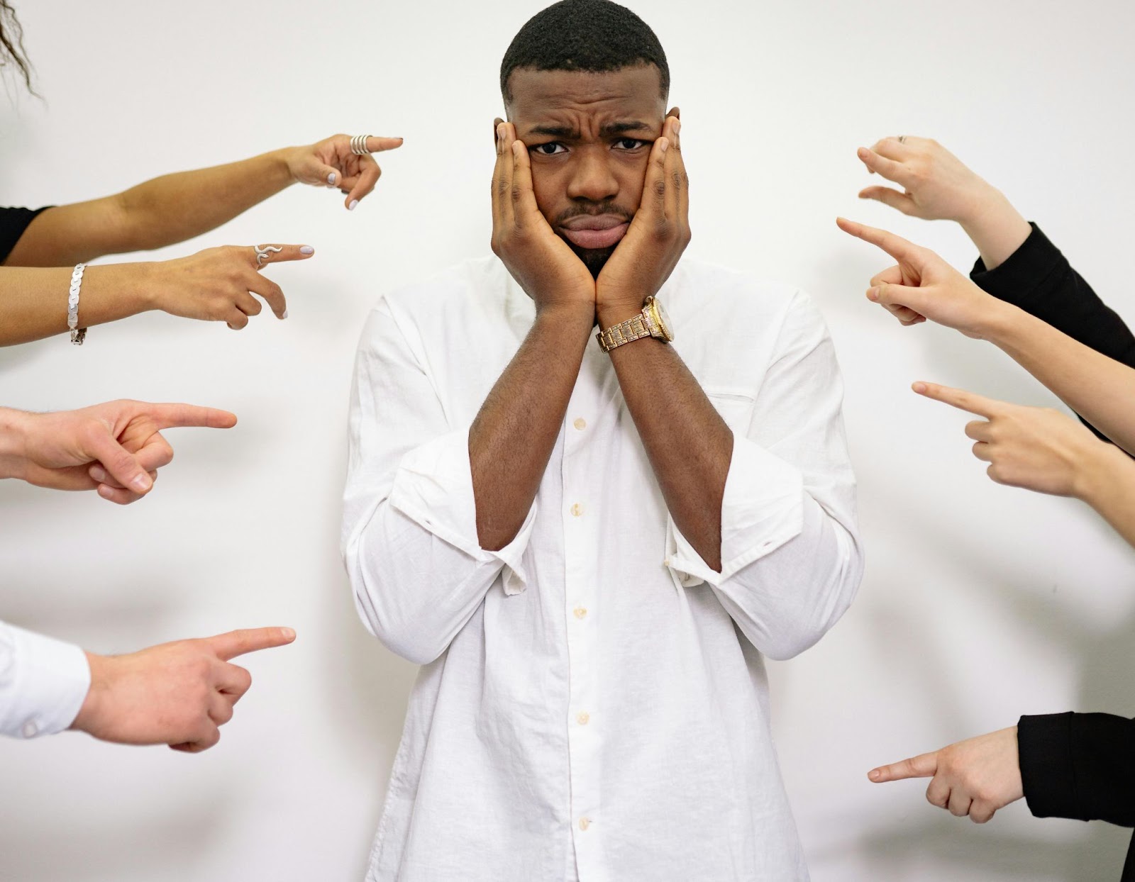 A man holding his head with his hands as fingers are pointed at him from all directions