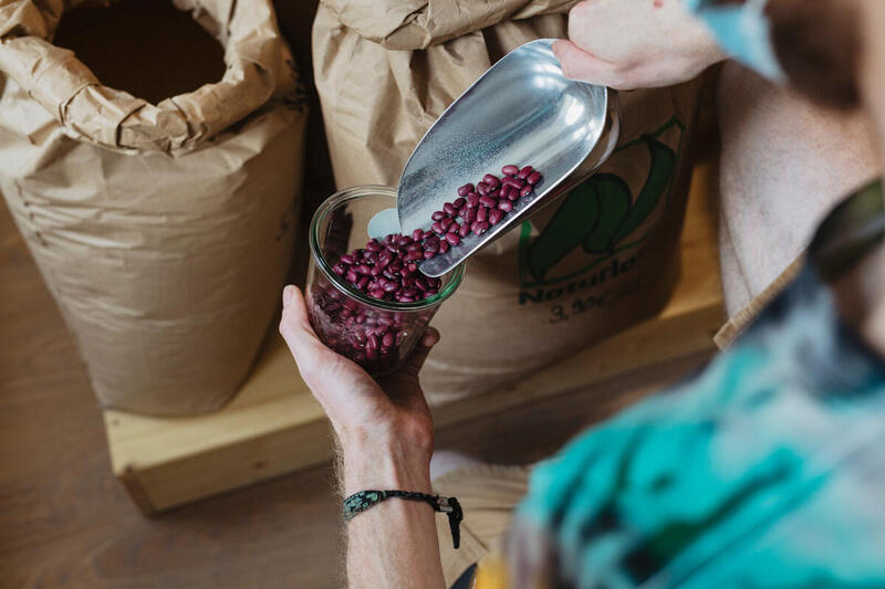 Someone pours beans into a glass jar, using a metal scoop