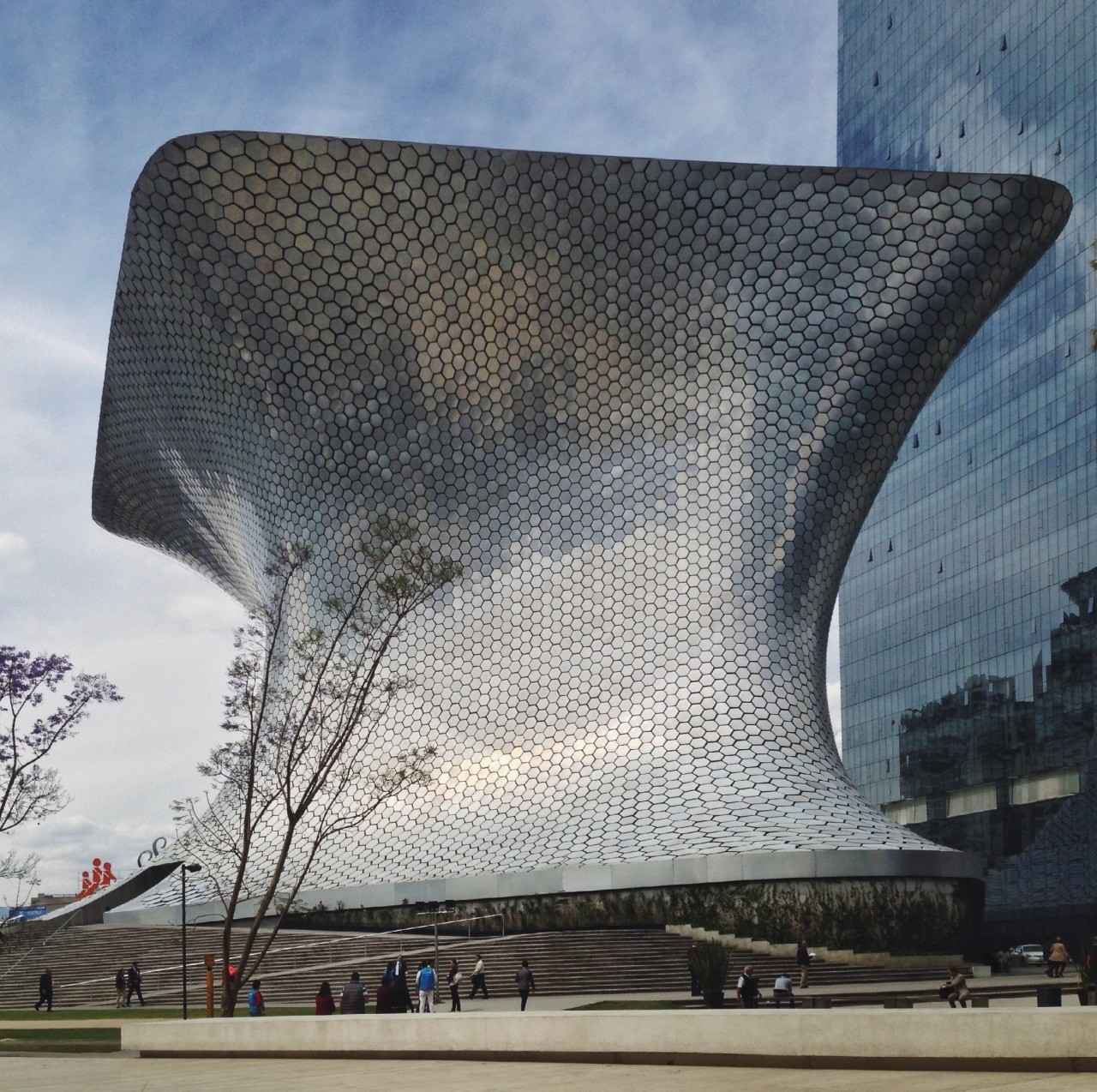 Architectural photography of a modern, futuristic building with a unique, curving shape covered in hexagonal tiles reflecting light.