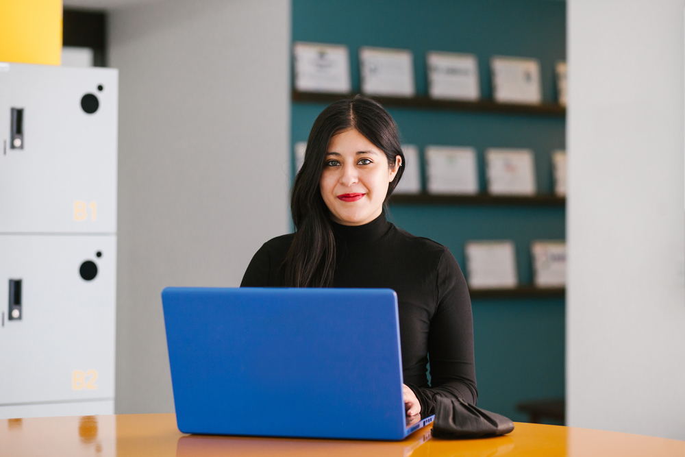 woman sitting at desk, using pc writing in notebook