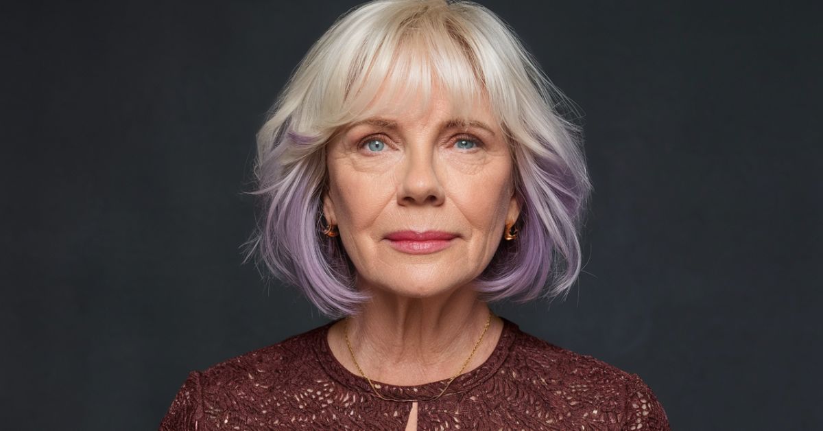 An older woman with purple hair styled in an Icy Blonde & Purple Bob, wearing a brown dress, exuding elegance and charm.