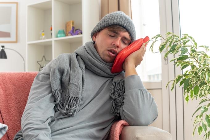 Dental pain relief at home with cold compress therapy showing person resting on couch in NYC apartment with winter attire