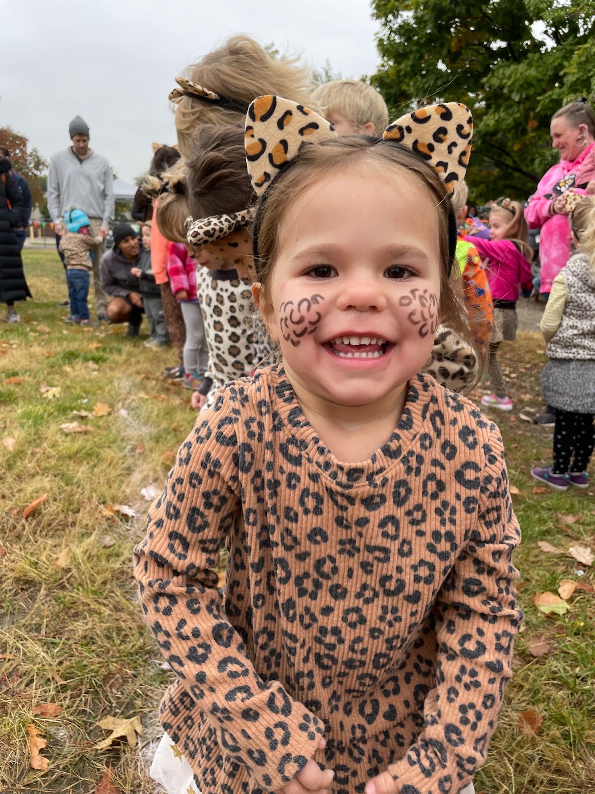 A 4-year old Gracie in a leopard costume with facepaint smiling in a park