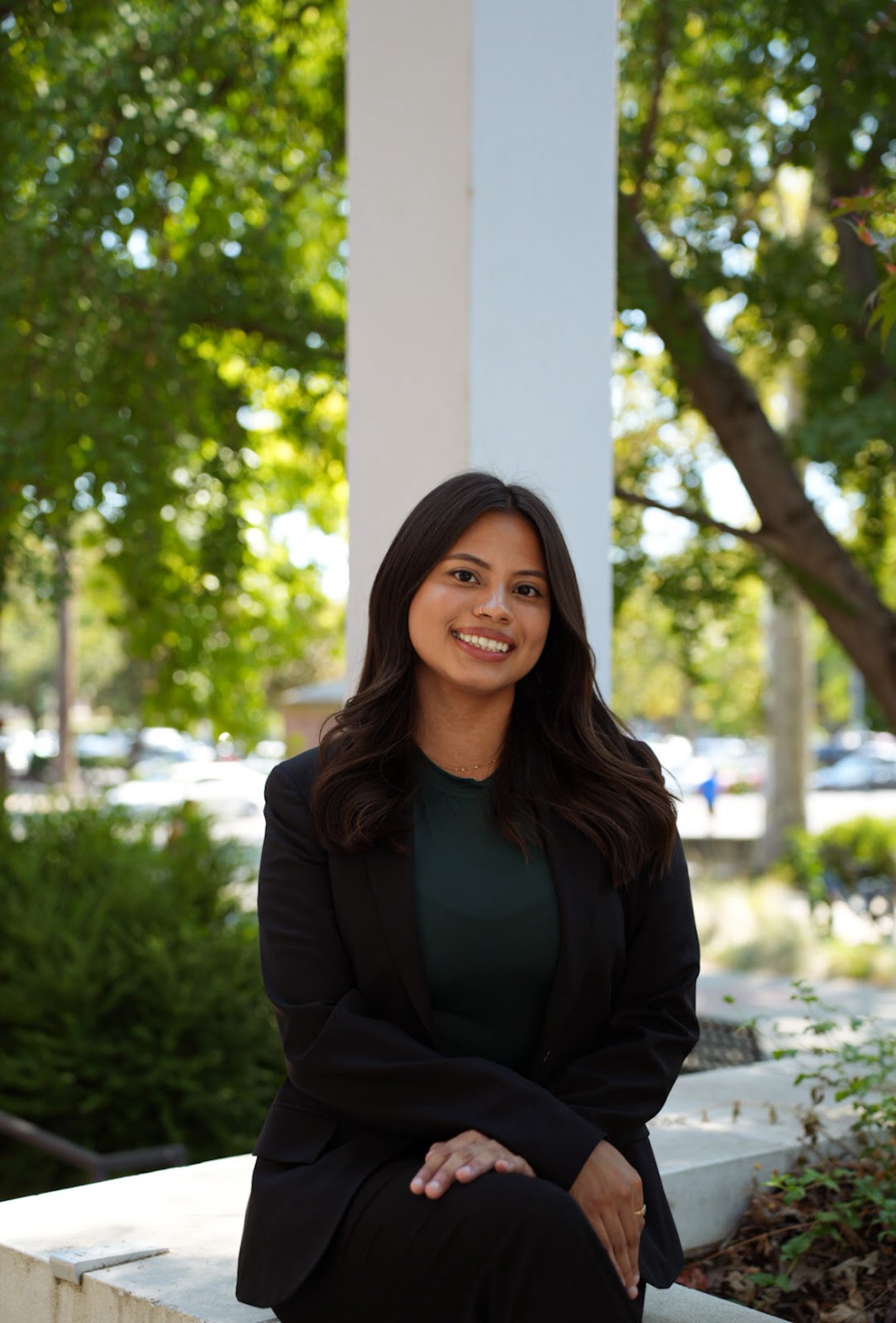 Esmeralda Barajas is sitting down and poses for a photograph outside of the performance arts building.
