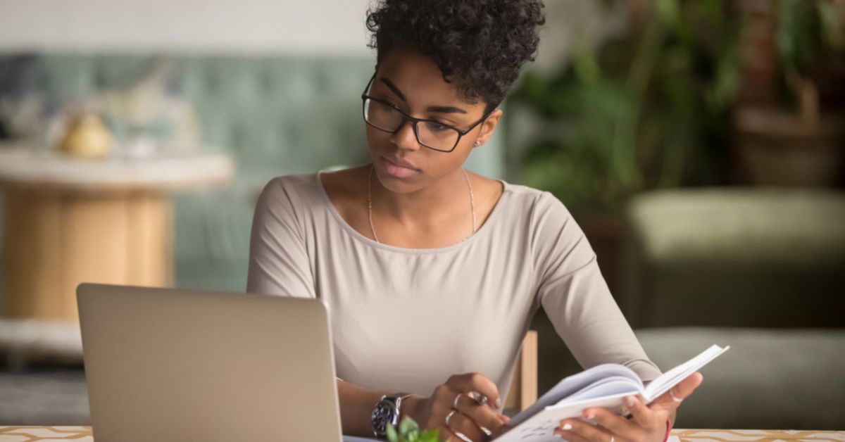 A woman in glasses is focused on her laptop, engaged in work with a determined expression.