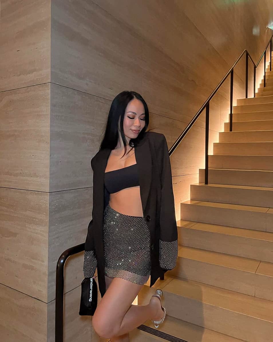 A woman wearing a sparkly mini skirt with a black bandeau top, a black blazer with sparkly trip, and silver heels