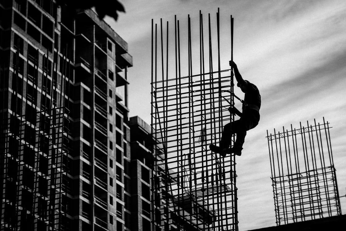 Construction worker climbing steel rebar on site, illustrating risk management system needs in high-risk industries.