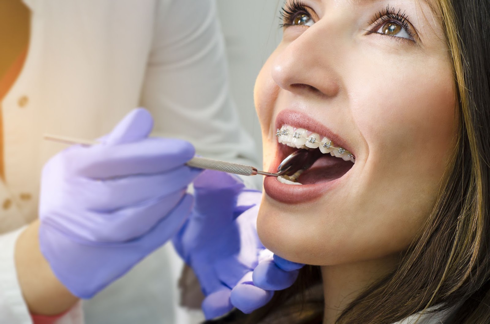 A young woman smiling while a dentist checks her braces.