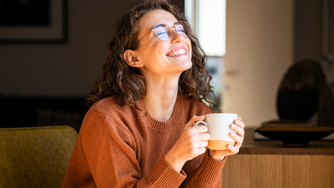 Woman enjoying coffee with a smile, symbolizing daily calm supported by CBG oil use