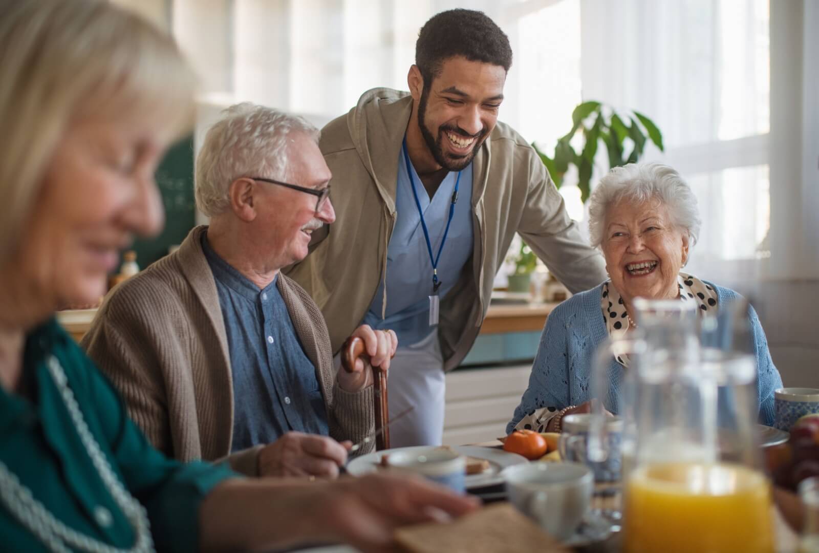 A group of seniors enjoying a meal together at a memory care community with dining assistance from a nurse.
