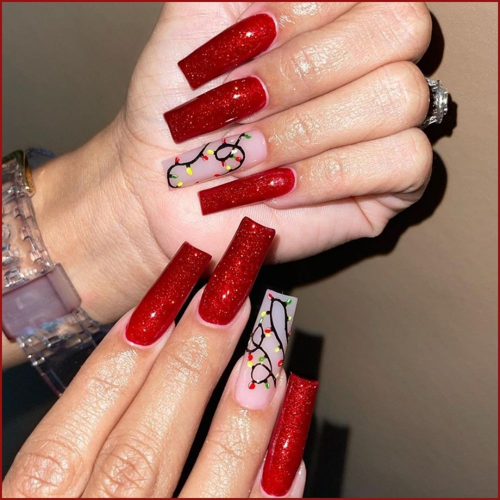 Close up of hands having Christmas red nails with Christmas Lights and Glitter Nails