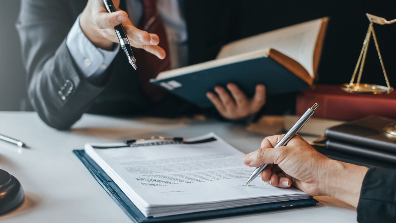 A legal meeting where two professionals are discussing documents; one points with a pen while explaining details to the other.