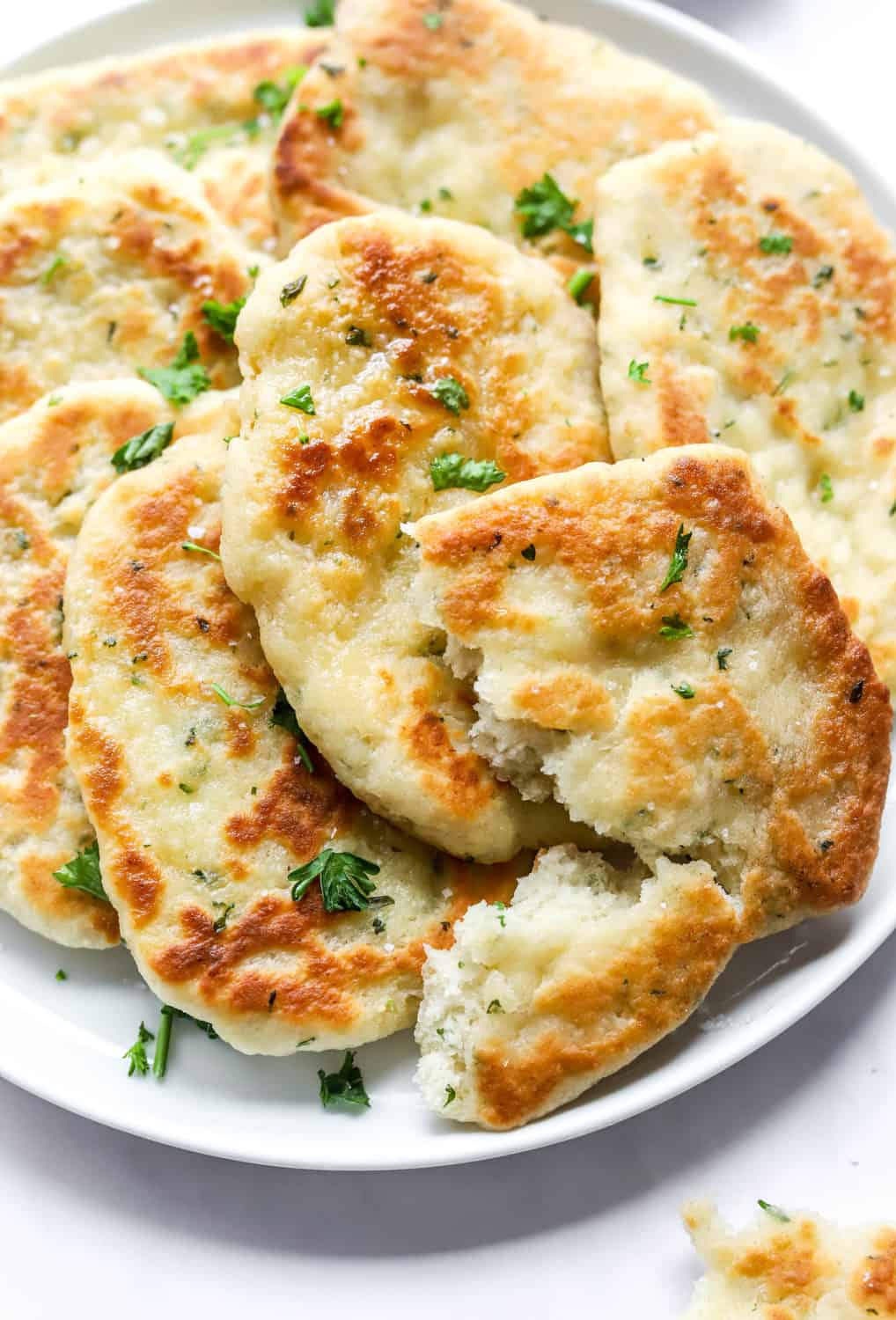 Plate of fluffy herb and butter bread with a piece torn open.