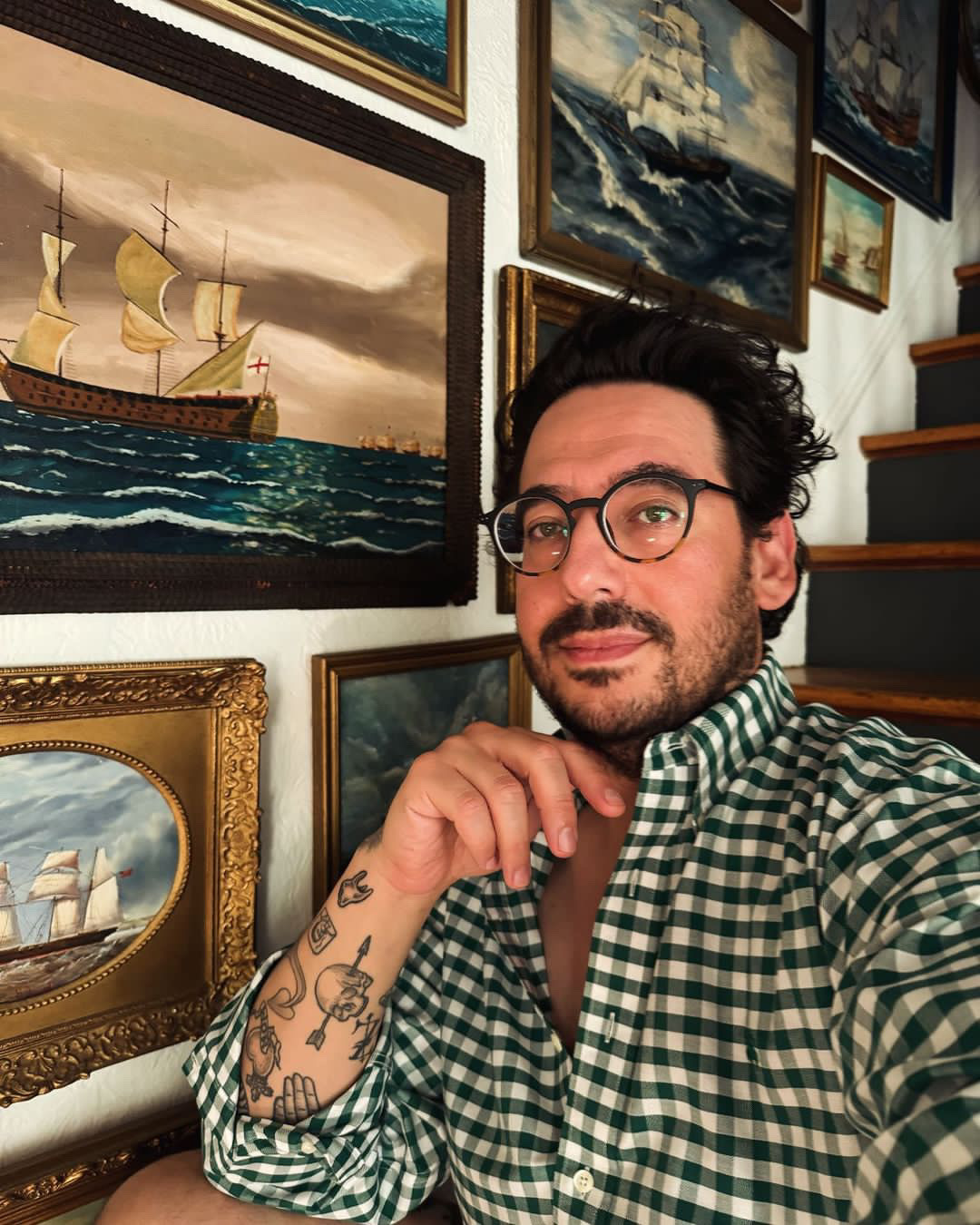 Memo taking a selfie in front of his gallery wall while wearing a black and white plaid shirt.