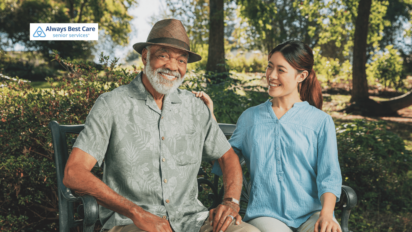 This image depicts a senior man and a caregiver in a park