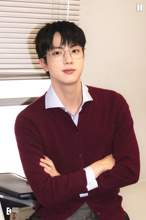 This contains an image of BTS Jin with glasses is posing for a photo in front of a computer desk