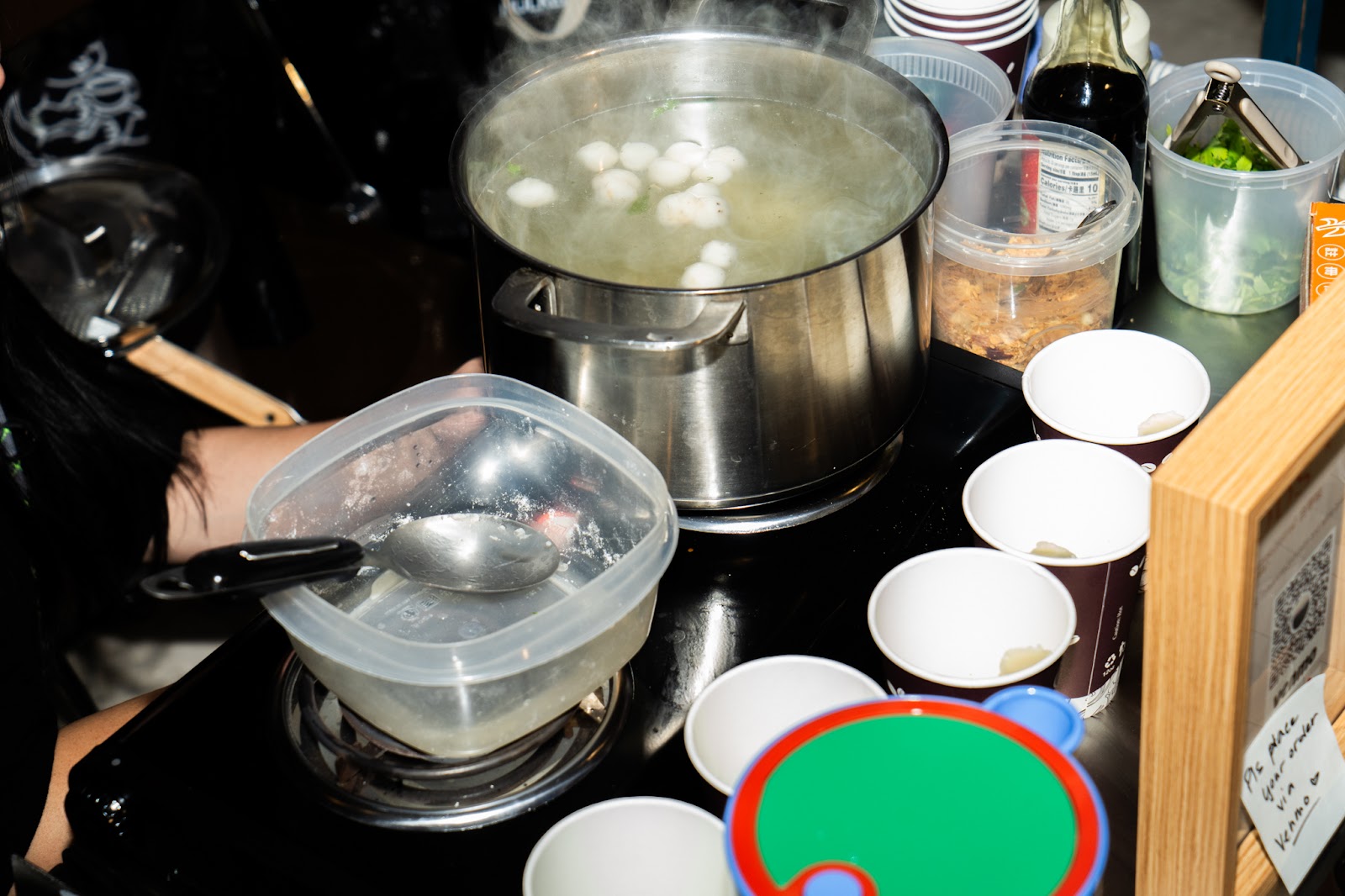 A vendor with a steaming pot of fish ball soup at a cooking station. 