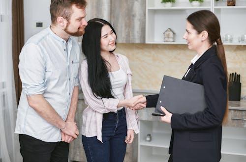 Free A young couple shakes hands with a real estate agent during a home tour or negotiation in a modern setting. Stock Photo