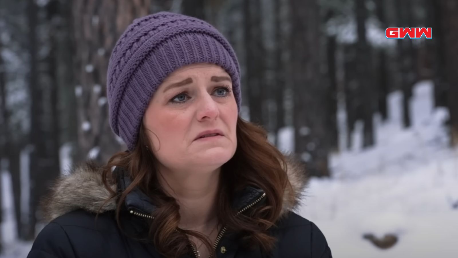 Robyn Brown outdoors in winter, wearing a purple beanie, looking concerned.