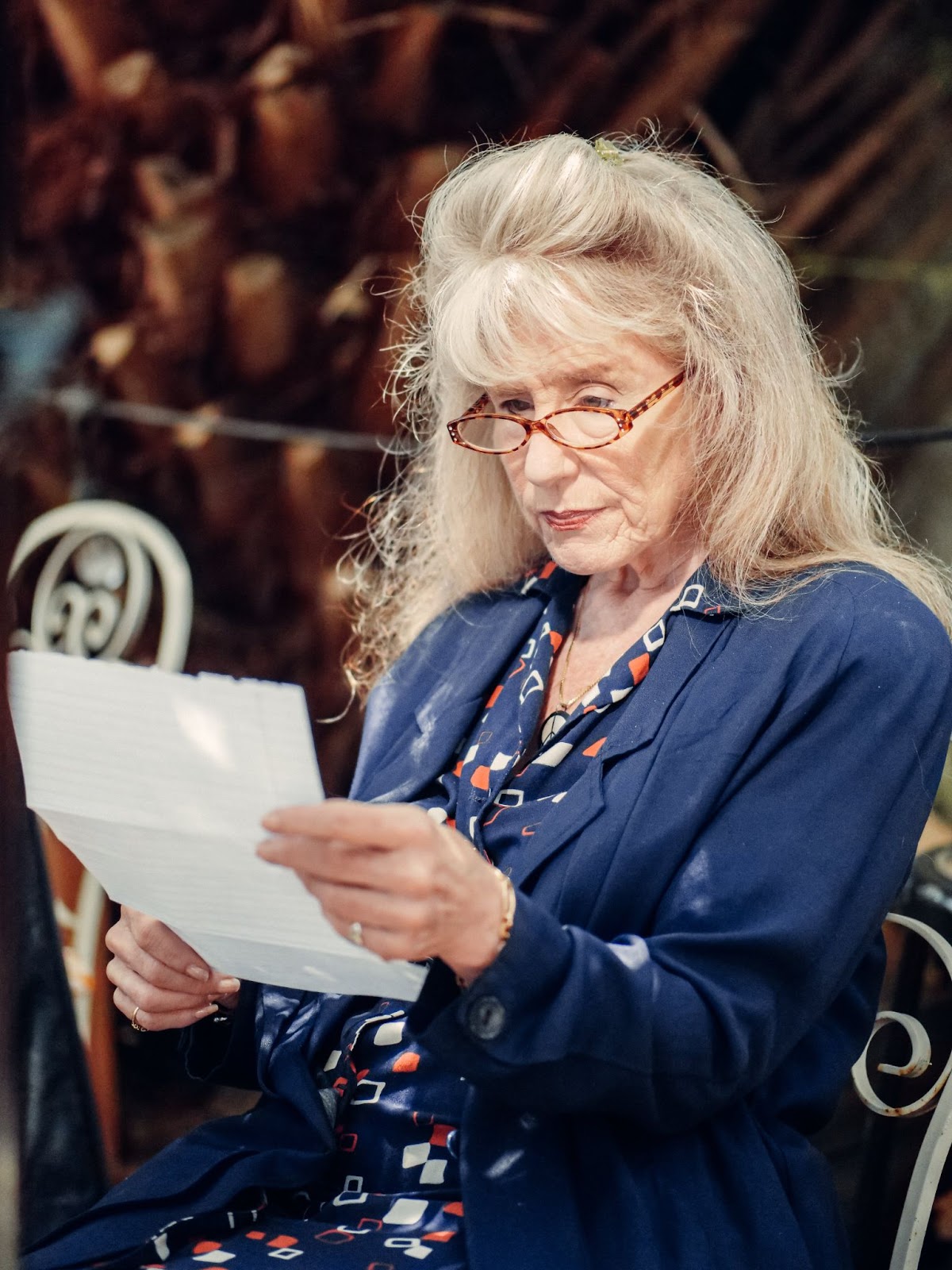 An elderly woman holding and looking at a piece of paper while sitting on a bench