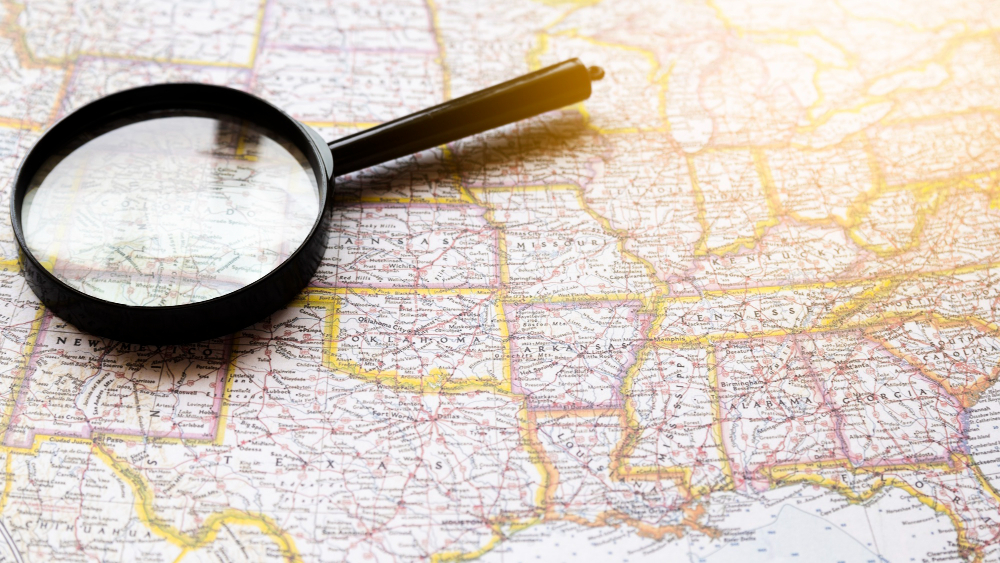 A map of the United States with a magnifying glass, representing state-specific requirements for FSBO legal processes.
